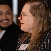 Event attendee smiling and chatting with those around her, other gentleman at table listening
